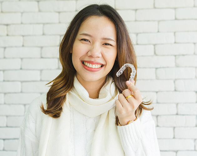 A brunette woman wearing white sweater holding invisalign