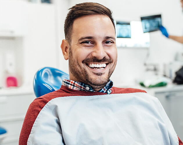 Man smiling at dentist chair thanks to dental crowns